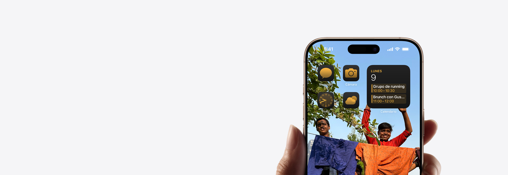 Una mano sostiene un iPhone 16 Pro con fotos, íconos y widgets en la pantalla de inicio.