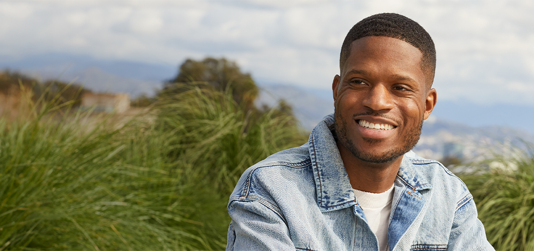 Justin smiling and sitting on an outdoor patio, with sky and trees in the background.