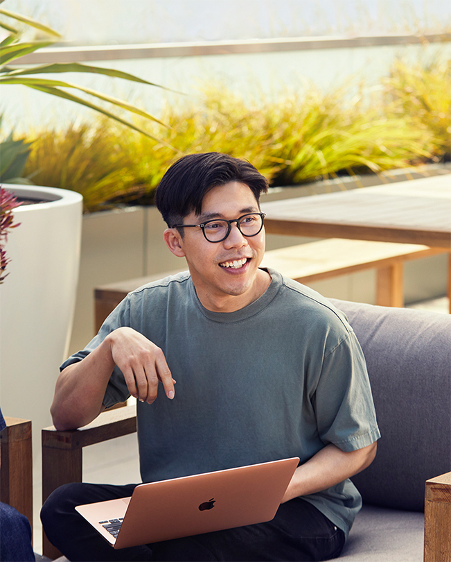 A smiling Apple employee sits outdoors with a MacBook.