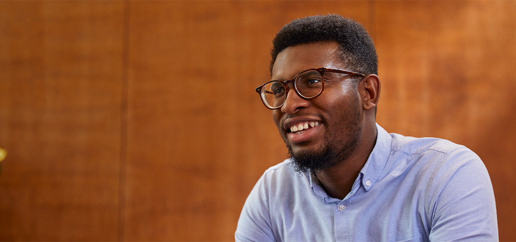 Chidi seduto che sorride distogliendo lo sguardo dall’obiettivo.