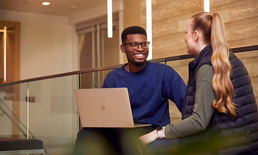 Chidi seduto che parla con una collega, appoggiando il suo MacBook sulle ginocchia .