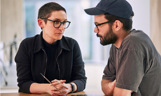 Sophie seduta a un tavolo che parla con un collega che usa un MacBook.