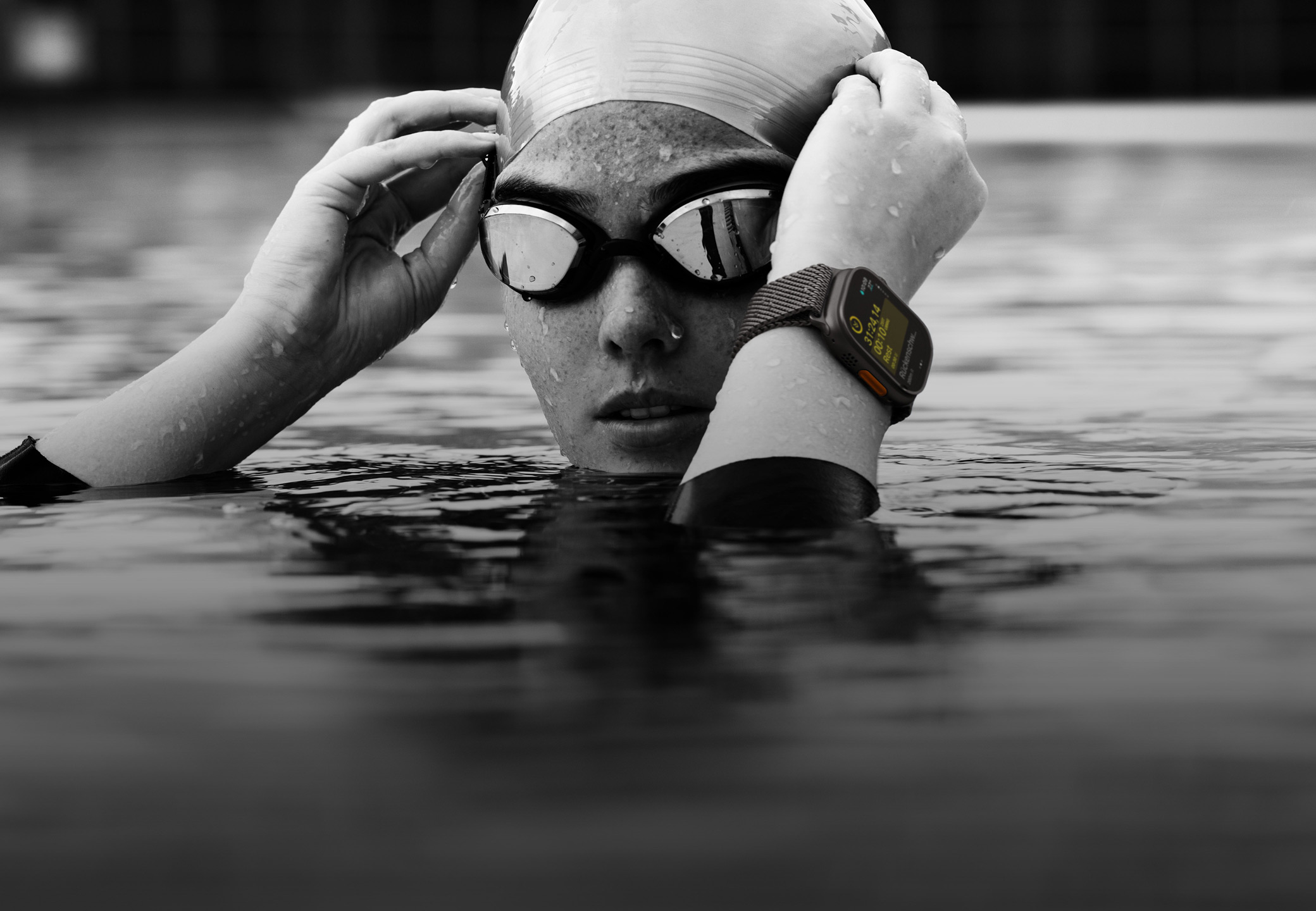 Kopf und Hände einer Schwimmerin über dem Wasser in einem Pool, die eine Apple Watch Ultra 2 trägt und ihre Schwimmbrille zurechtrückt.