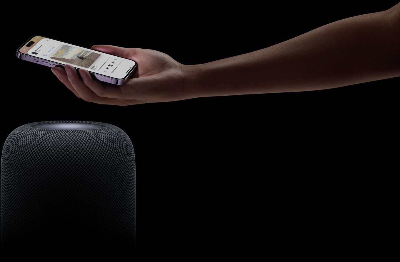 A hand coming in from the right side of the page holds an iPhone above a HomePod speaker