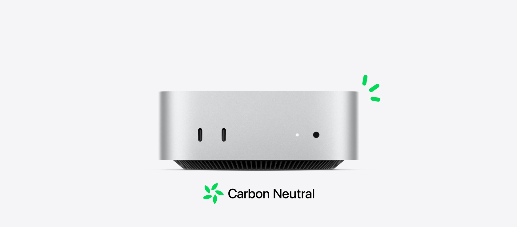 Imagem da frente do Mac mini prateado, mostrando as portas na frente, com pequenos detalhes em verde ilustrando a neutralidade em carbono.